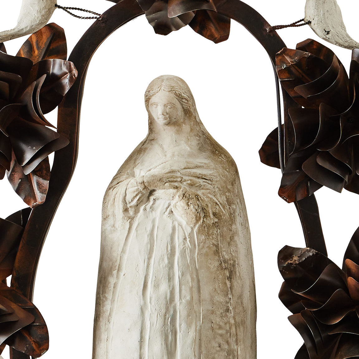 The face of a hand carved stone statue of the virgin of Guadalupe surrounded by an aura and halo of iron flowers and stone birds.