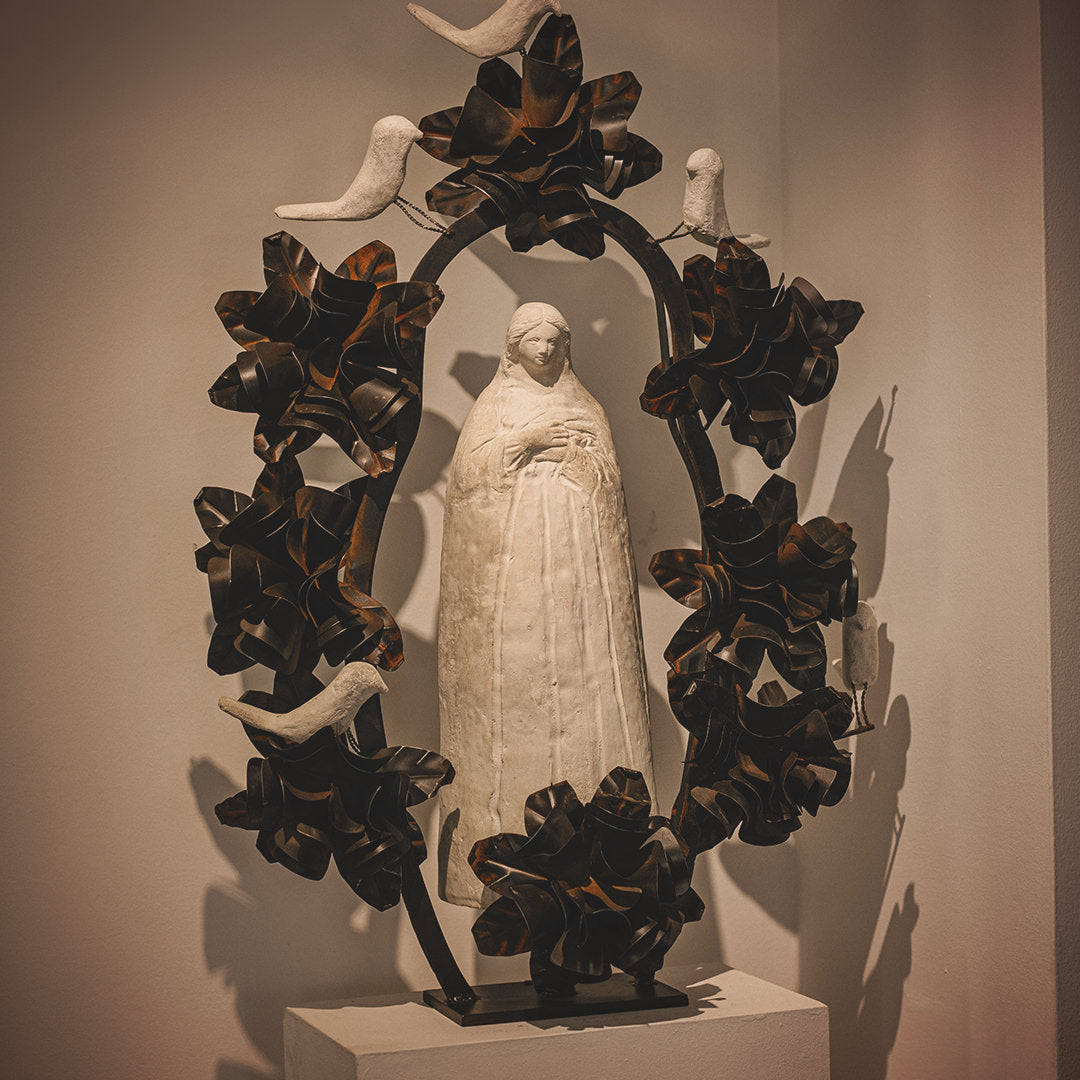 A stone statue of the virgin of Guadalupe surrounded by an aura and halo of iron flowers and stone birds.