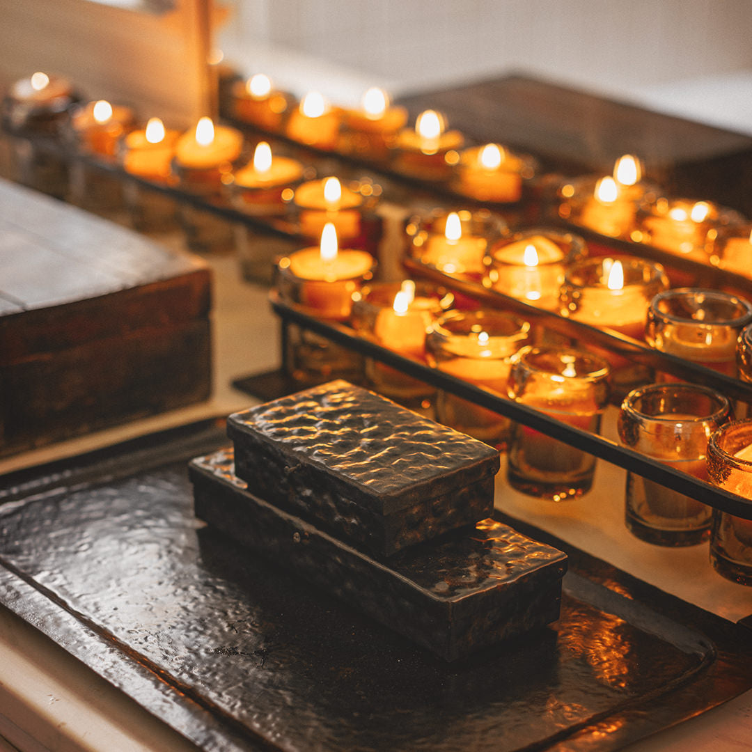 Several lit candles inside glasses. Two iron boxes on top of an iron try.