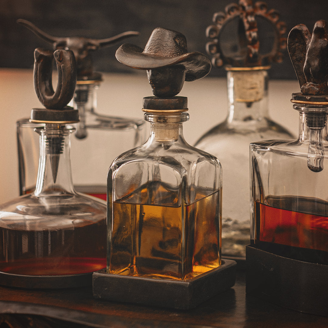 Five clear decanters filled with liquid, each one with a different shape iron topper and a iron tray.