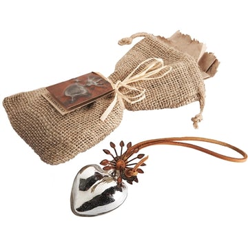 Blown glass heart with platinum finish on leather cord and a brown bag. White background.