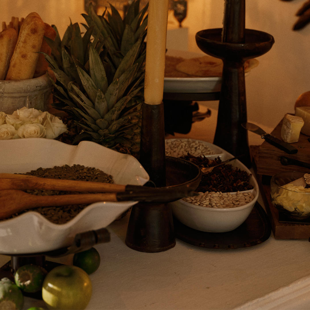White bowls with seeds, bread, pineapples , iron candle holders and cheese together.