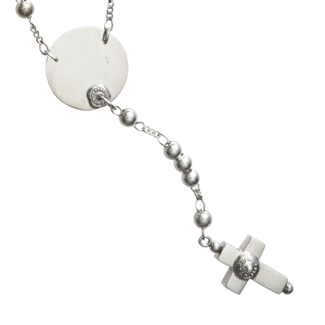 A delicate silver necklace with a fine chain design and a circle near the end with a cross charm in the end, displayed on a plain background.