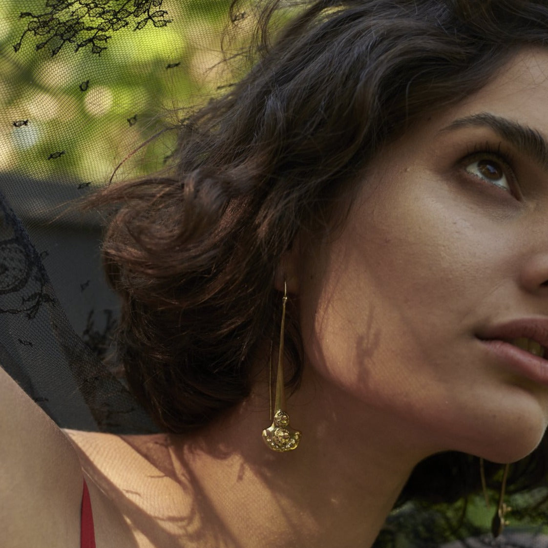 Part of a woman face. She is looking up. She is wearing a bronze hook earring. The bottom of the earring has a half circle or open fan shape. The earring has two seals. The earring is a the center of the picture.