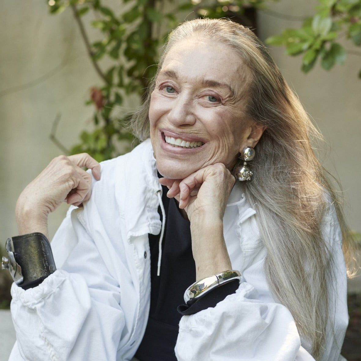 An older woman in a black shirt and white jacket smiling while wearing silver jewelry.