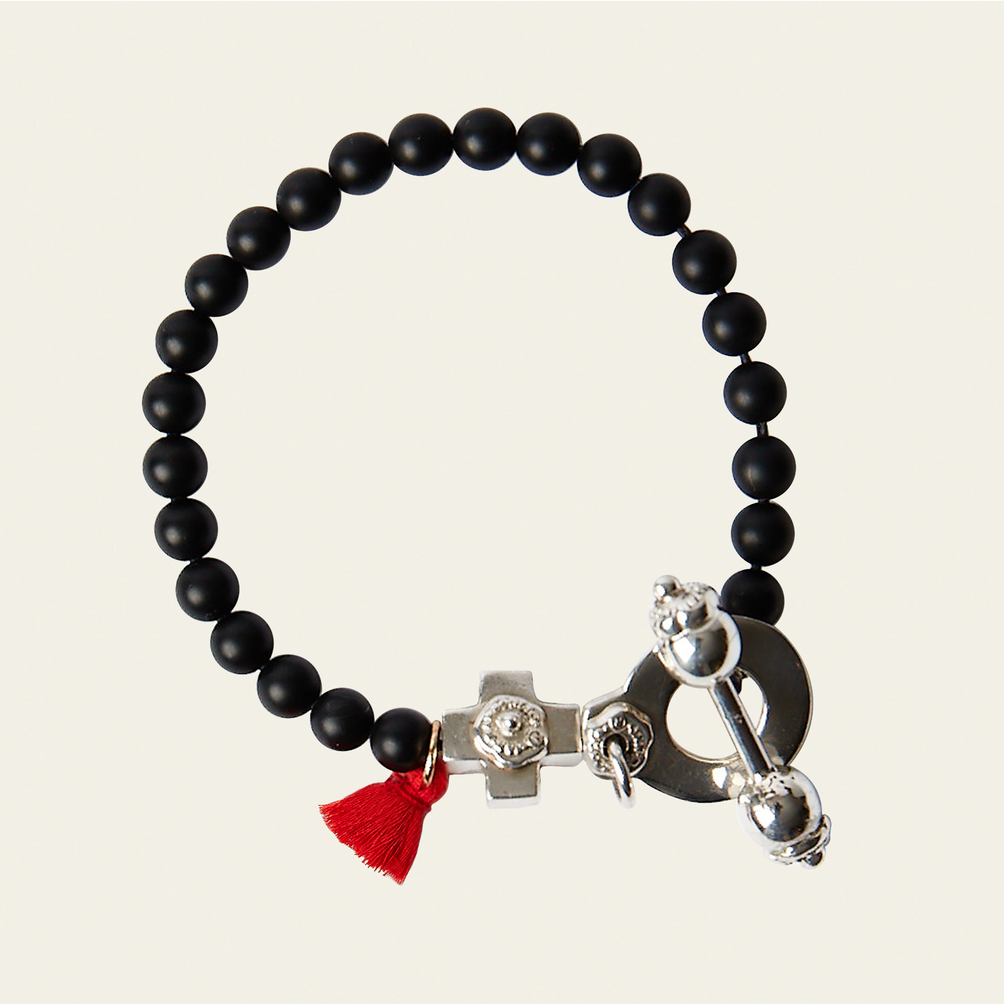 A black bead bracelet with a red string charm and a silver cross charm. Plain background.