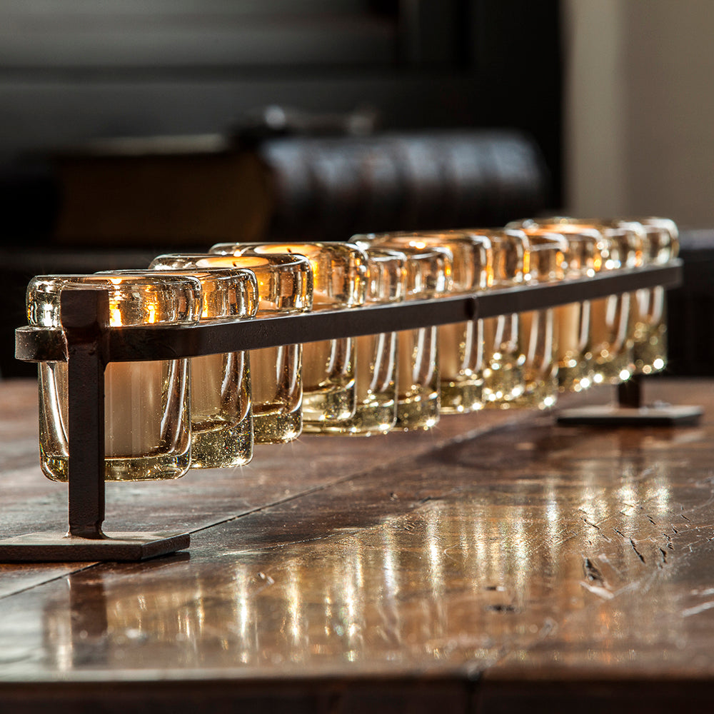 Wax cast railroad with mouth blown glass votive holders on forged iron stand. Placed on top of a wooden surface.