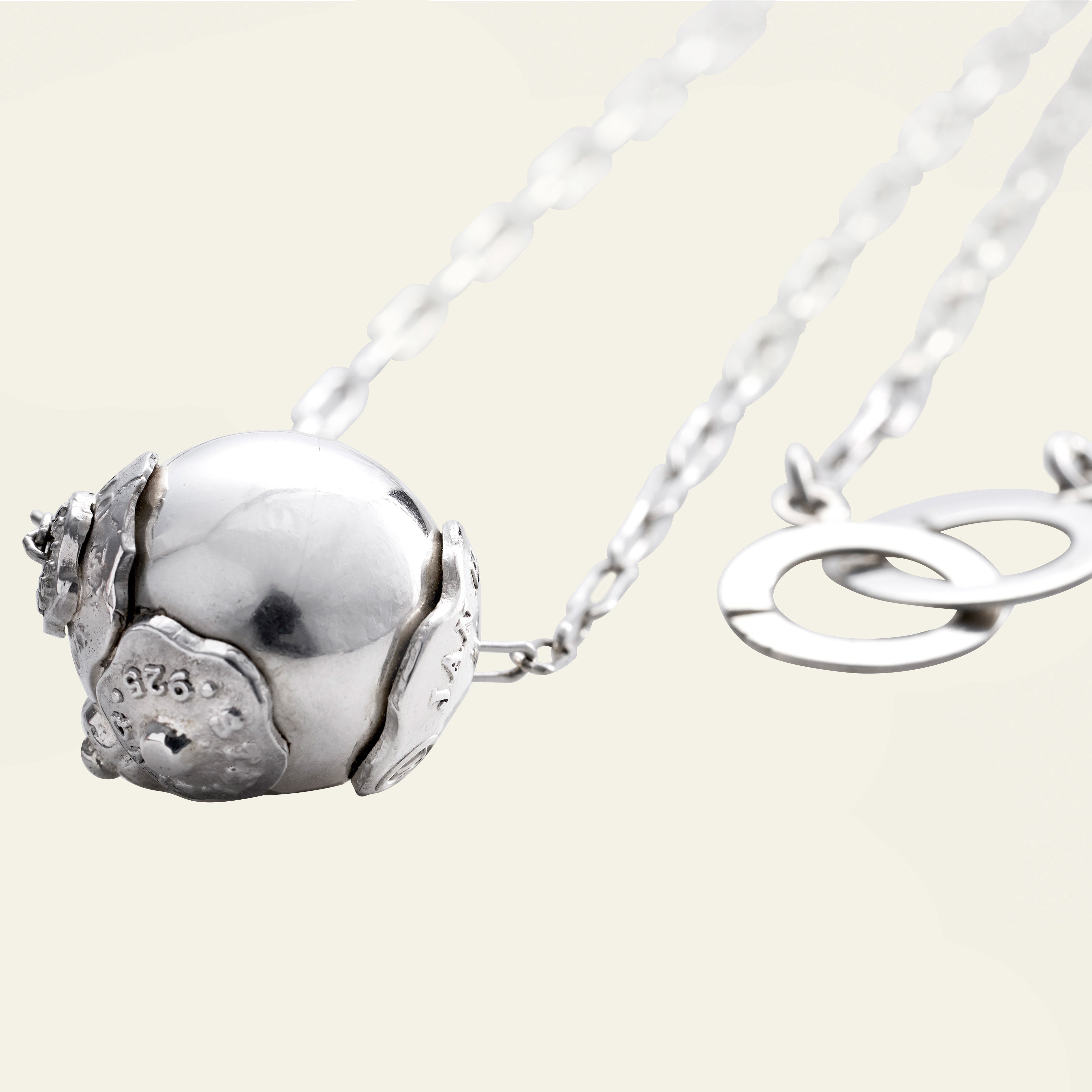 A silver bead with three seals and a delicate silver chain behind. A simple background.