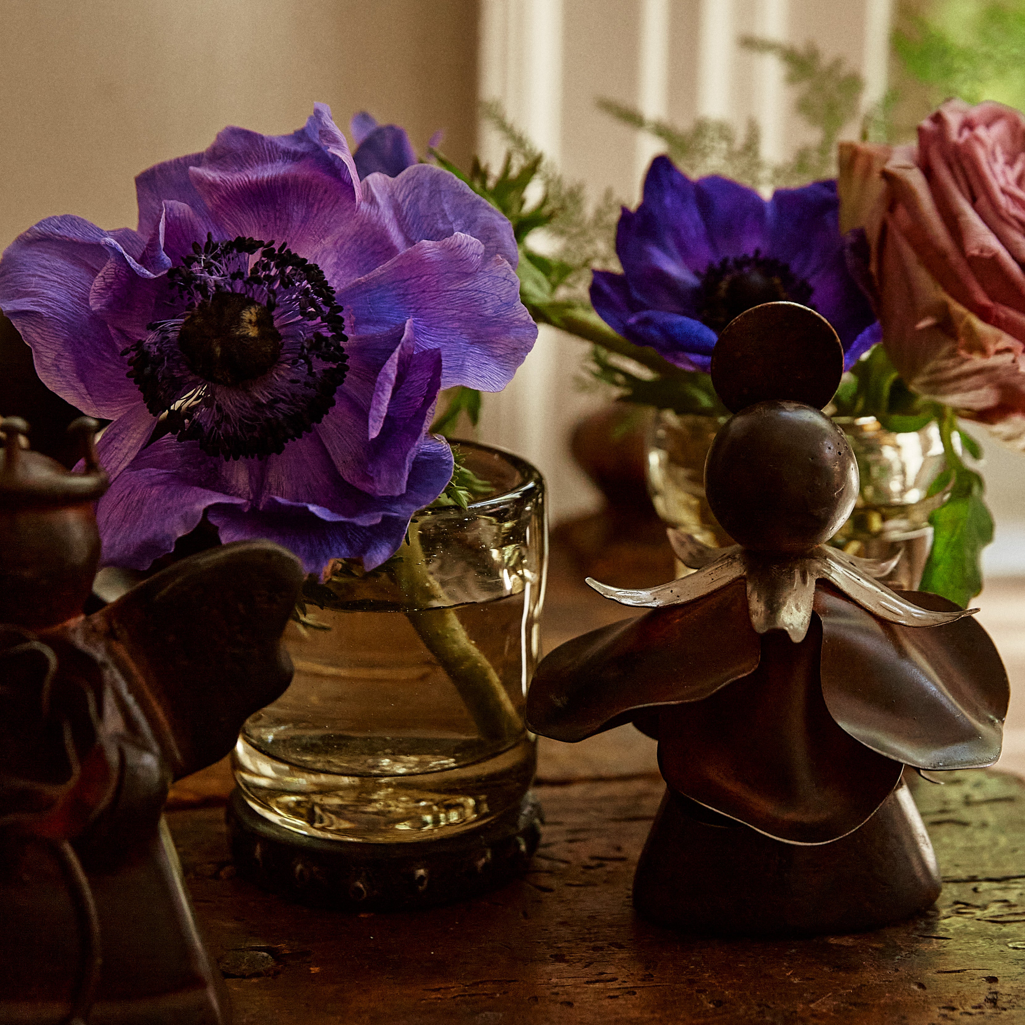 Two purple flowers and a rose in some glasses with iron coaster. Two iron angels in front.