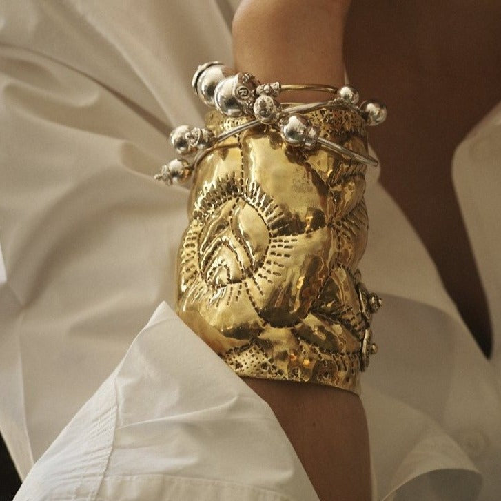 A wrist with a golden cuff and silver bracelets.