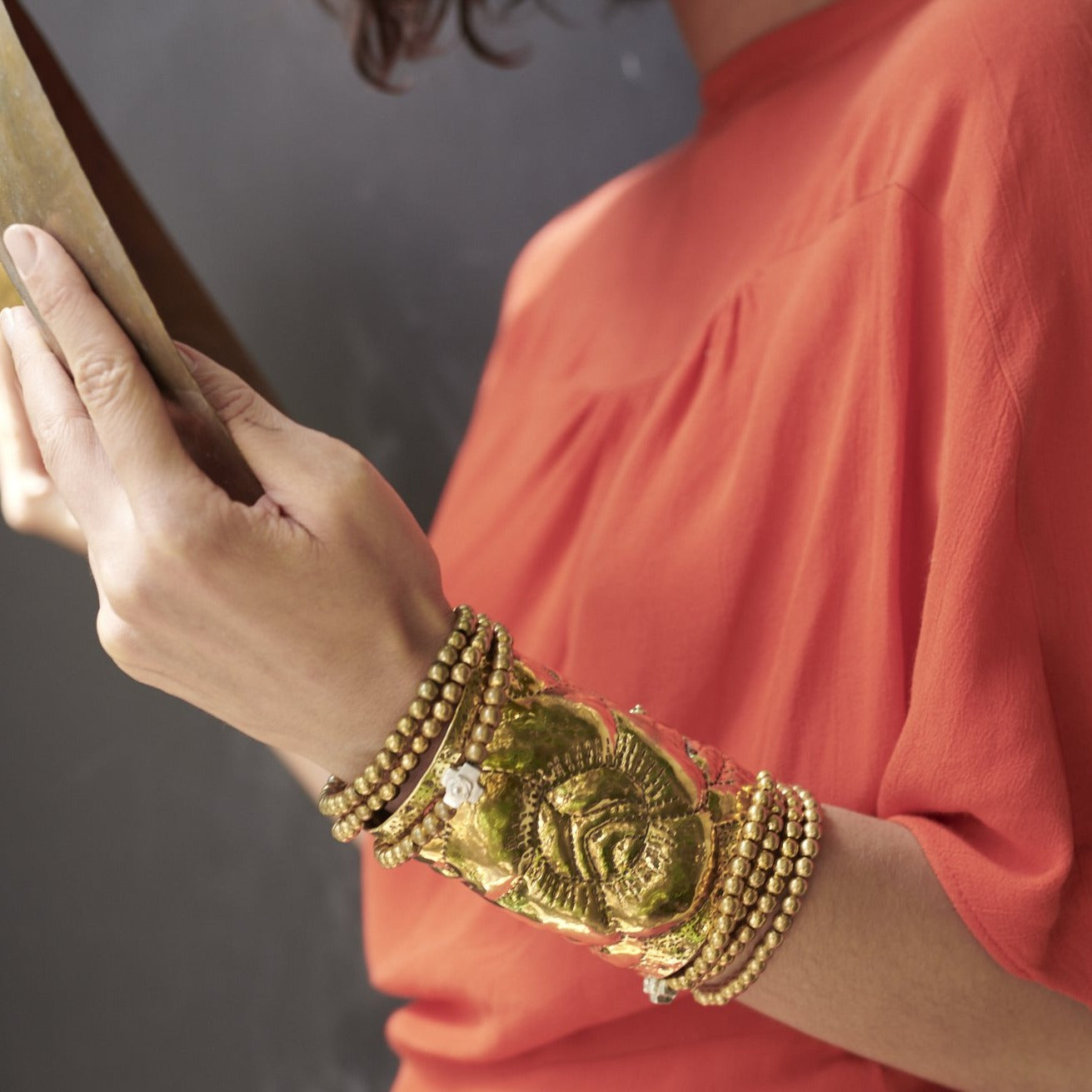 A woman holding a book. In her wrist is a bronze cuff with an engraved rose and several bronze beads bracelets.