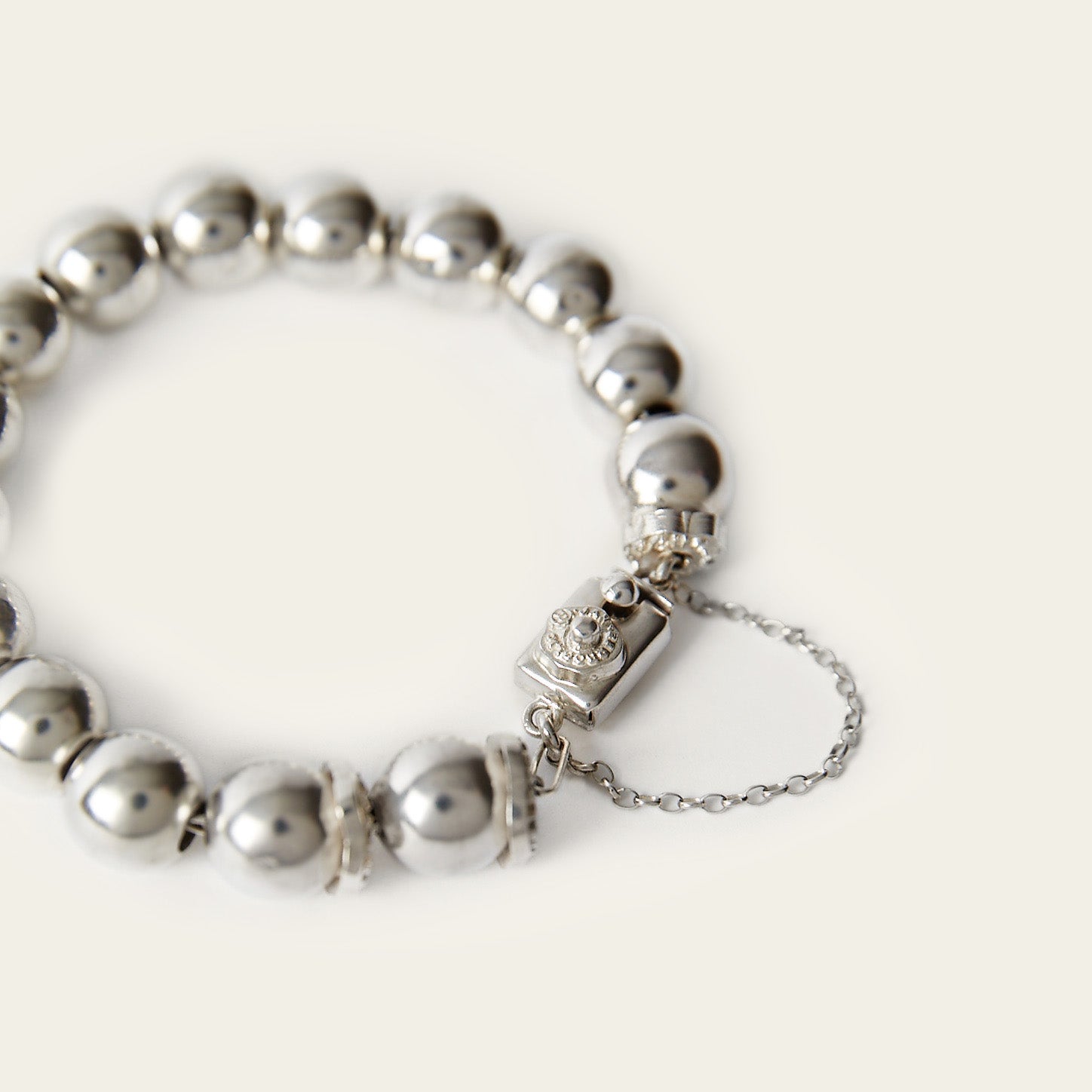 A silver bead bracelet with a rectangle and a delicate chain. Plain background.