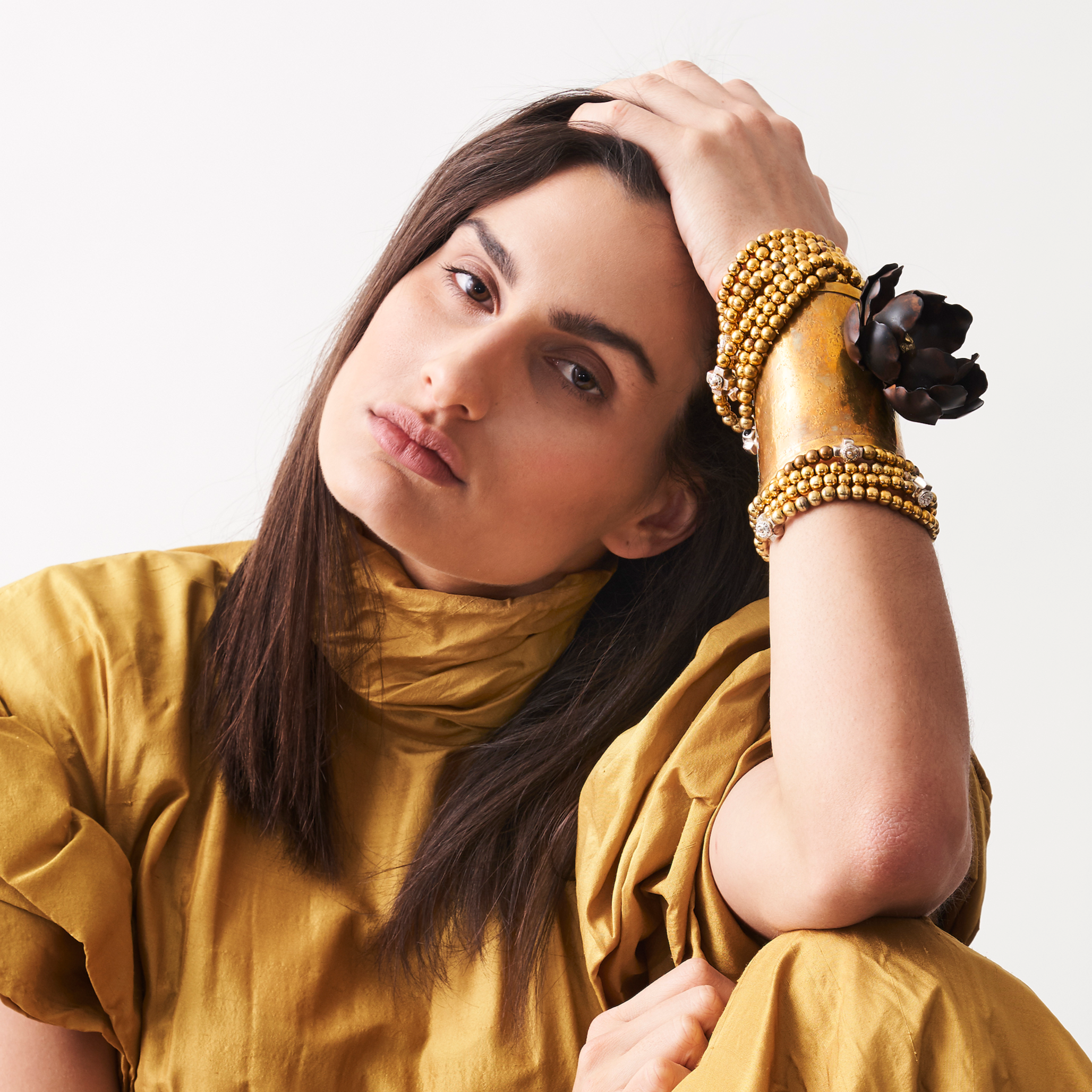 A woman resting her hand in her head.
In her wrist are several bronze beads bracelet and a cuff with a dark metal rose.
