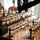 A hand placing a candle. Several candles inside glasses in an iron holder.