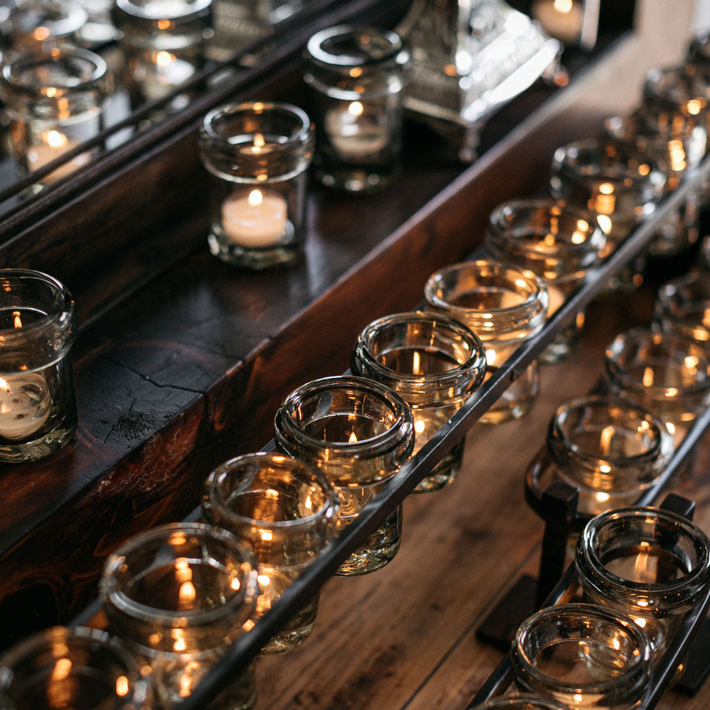 Several lit candles inside glasses. Some are being held by an iron and others are placed on top of the wood.