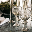 Two  clear mouth blown goblets with  laurel engraving. In the background are several clear glass flutes.