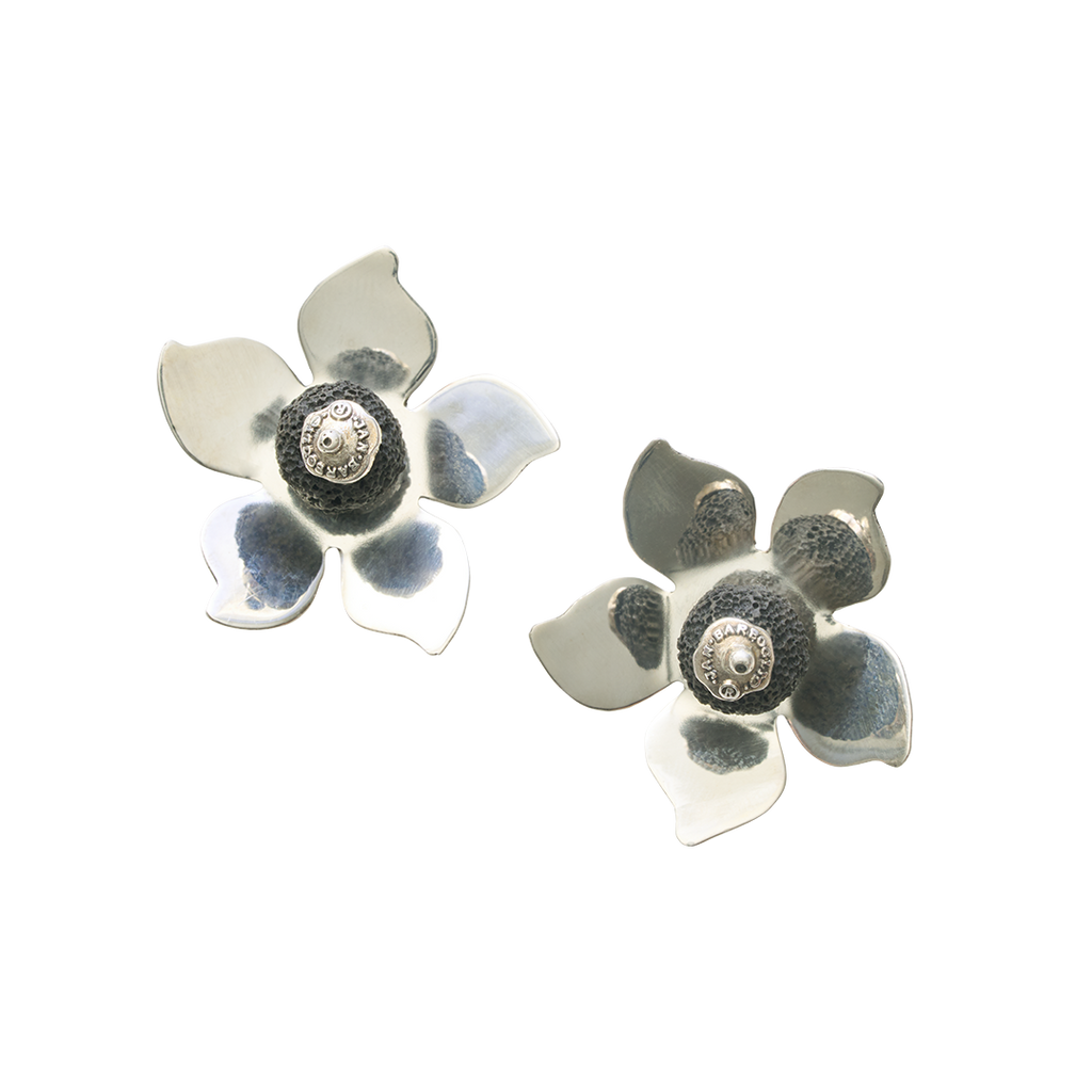 A pair of silver flowers earrings with a volcanic stone in the center. On top of the stone is a silver seal.