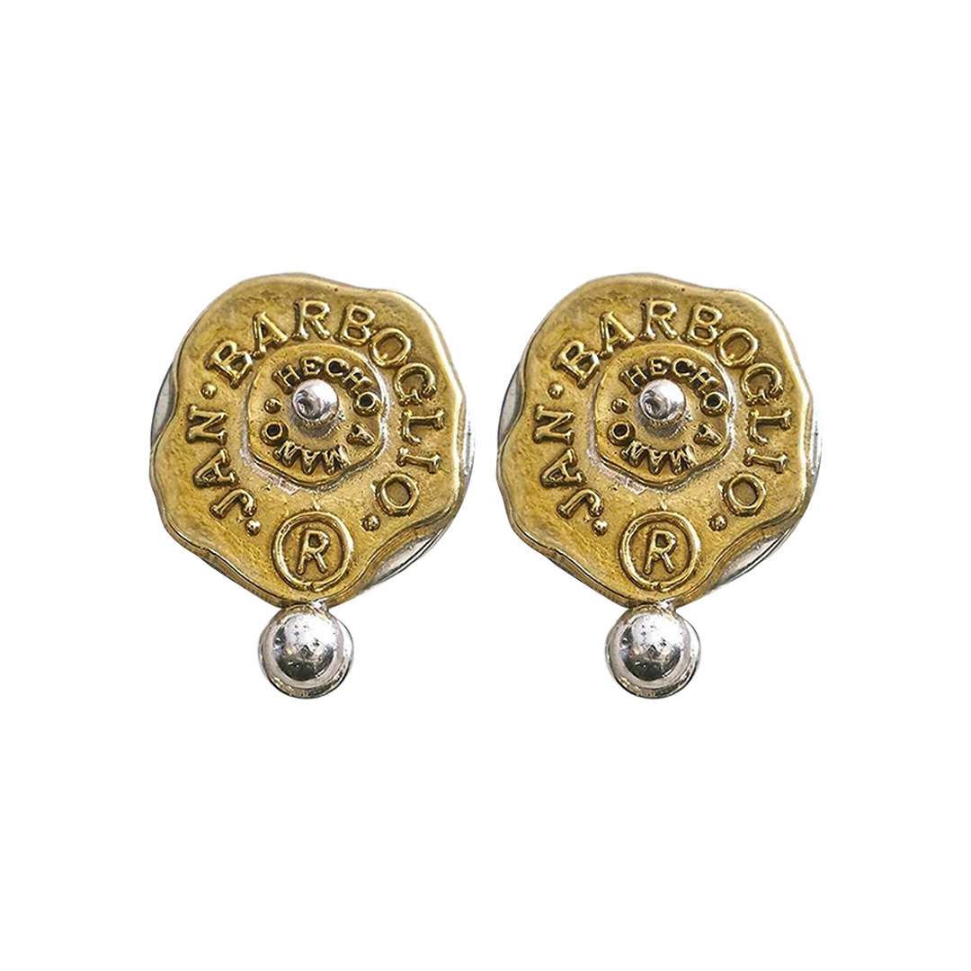 Gold and silver almost circular earrings with a seal that includes the designer's name. A small ball is under the seals and another one is in the center of the seal.