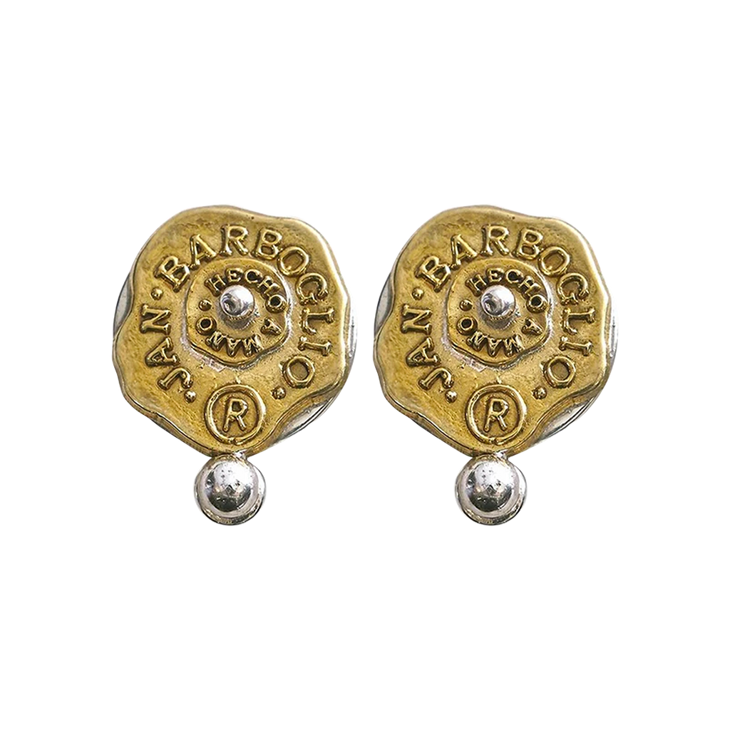 Gold and silver almost circular earrings with a seal that includes the designer's name. A small ball is under the seals and another one is in the center of the seal.