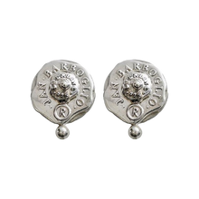 Silver earrings with a seal. The seals says thee name of the designer and place of origin. A small silver bead in under the seal.