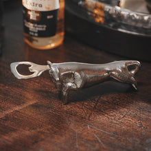 A nickel plated iron cast longhorn with stainless steel bottle opener on a wood surface. On the background is a beer bottle.