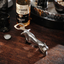 A nickel plated iron cast longhorn with stainless steel bottle opener on a wood surface. Behind it is a beer bottle and on the background part of a tray.