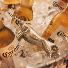 A nickel plated iron cast longhorn with stainless steel bottle opener on top of ice surrounded by beer bottles.