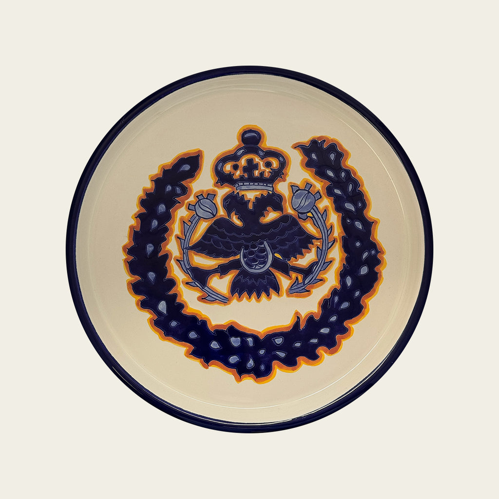 A ceramic platter with hand painted double eagle in blue and orange. White background.