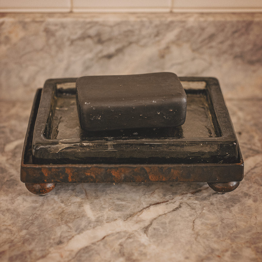 A hammered iron tray with a glass surface and a black soap on top.