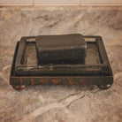 A hammered iron tray with a glass surface and a black soap on top.