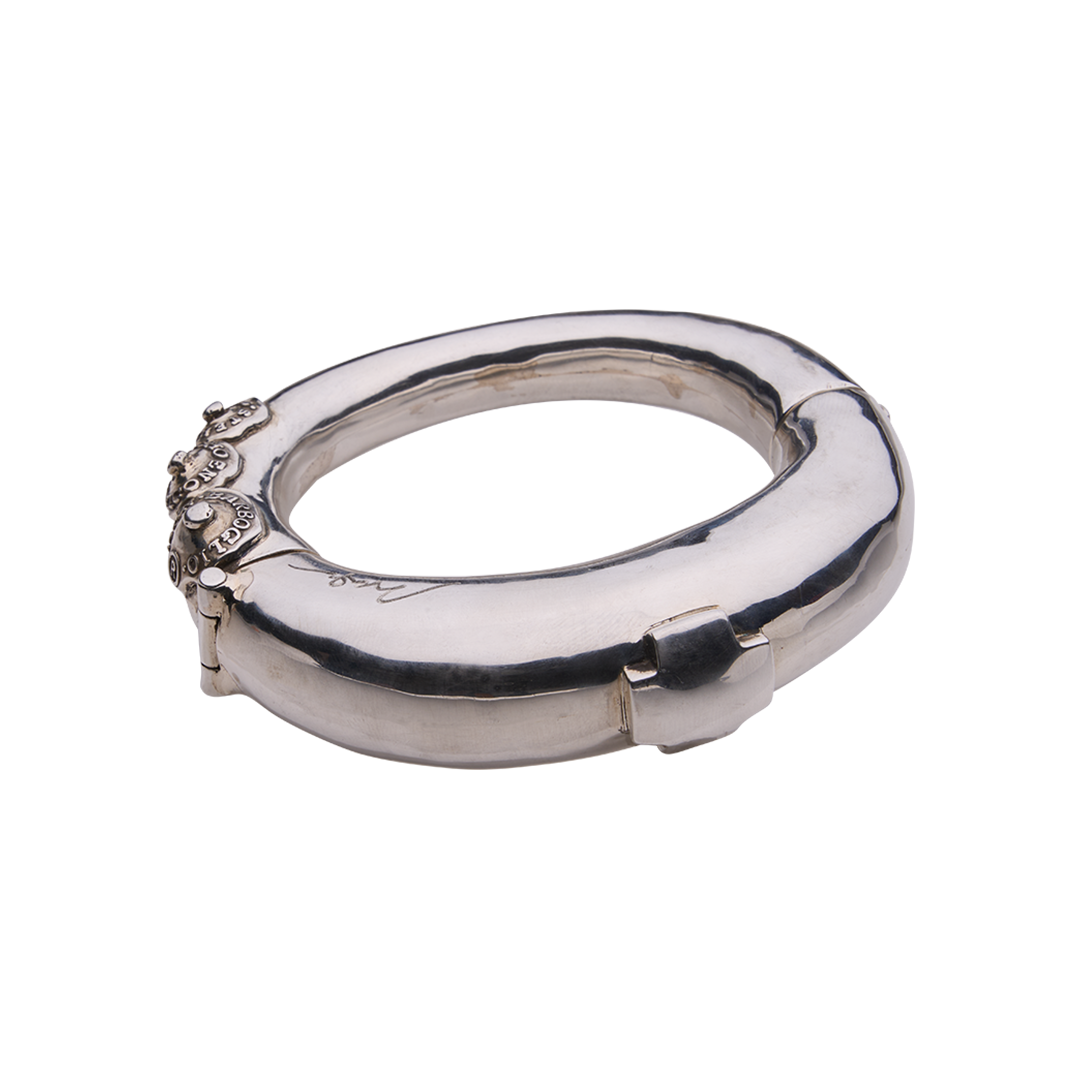 A silver bracelet featuring a cross and three seals with the designer name on the left.