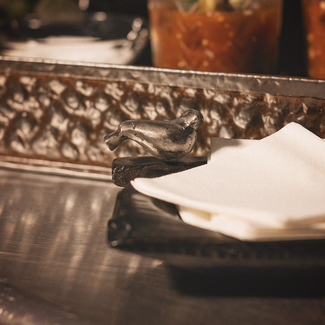 Half of a hand carved small rectangular primitive wood bowl showing only one iron bird and napkins inside.