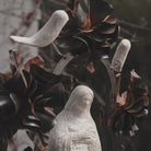 A close up to the face of a stone statue of the virgin of  Guadalupe surrounded by an aura and halo of iron flowers and stone birds. 