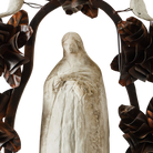The face of a  hand carved stone statue of the virgin of  Guadalupe surrounded by an aura and halo of iron flowers and stone birds. 