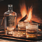 A tray with two glasses and a alcohol bottle and some pistachios. On the background is a fire.