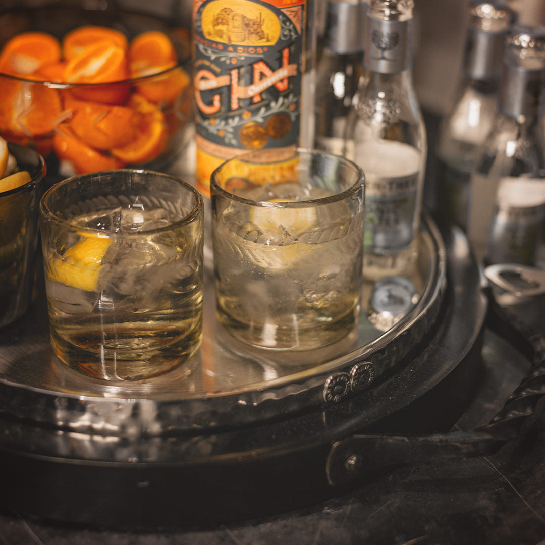A tray with two glasses, a bowl with oranges and some bottles.