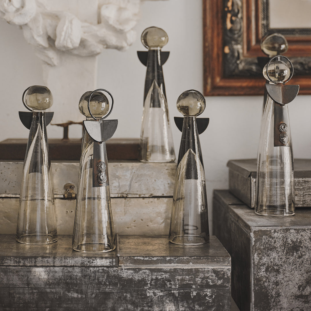 Several  mouth blown glass angels  with iron wings and halo standing next to each other  on top of a grey and white surface.