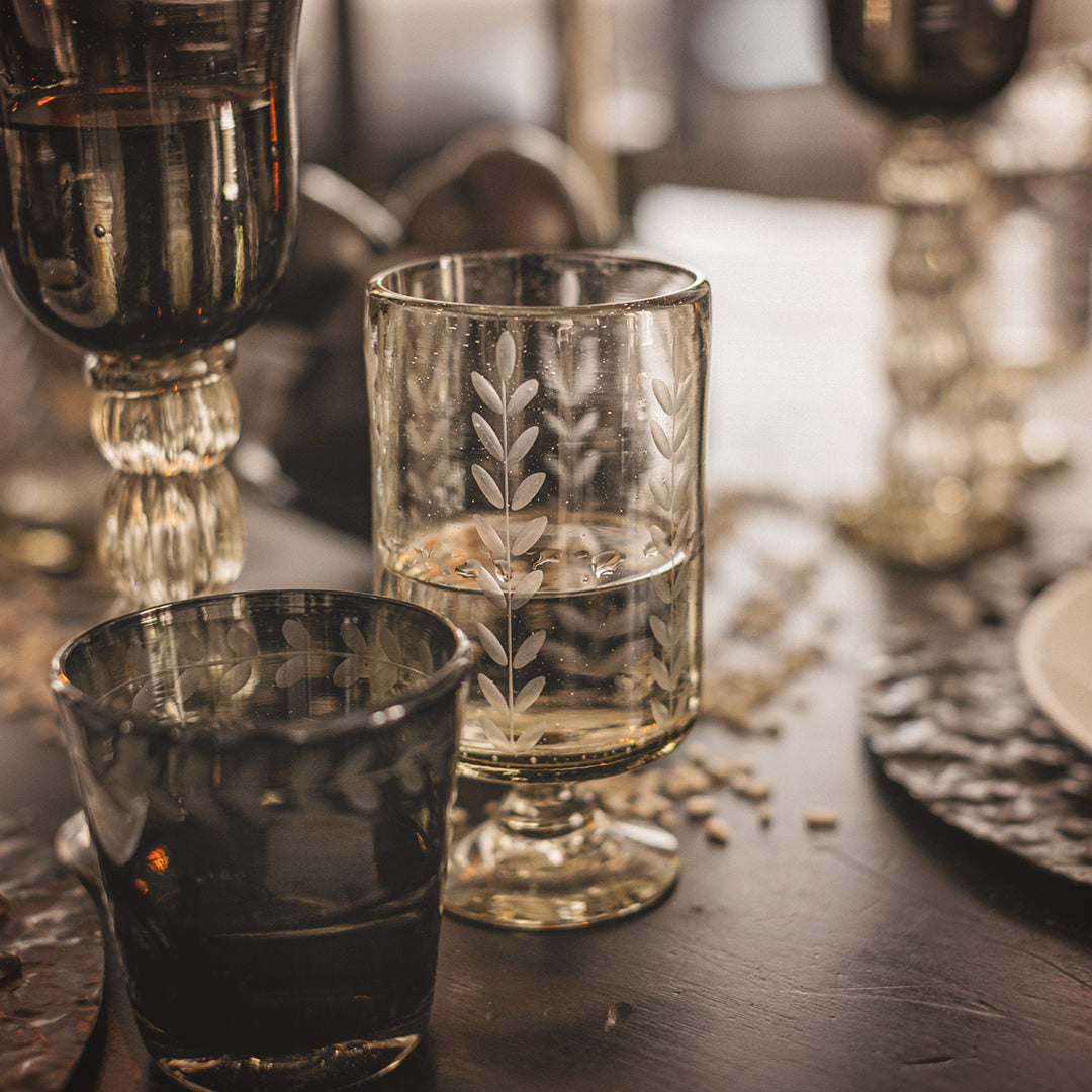 A table with a mouth blown glass engraved with vertical laurel leaves, a smoke color glass and a smoke colored cup. 