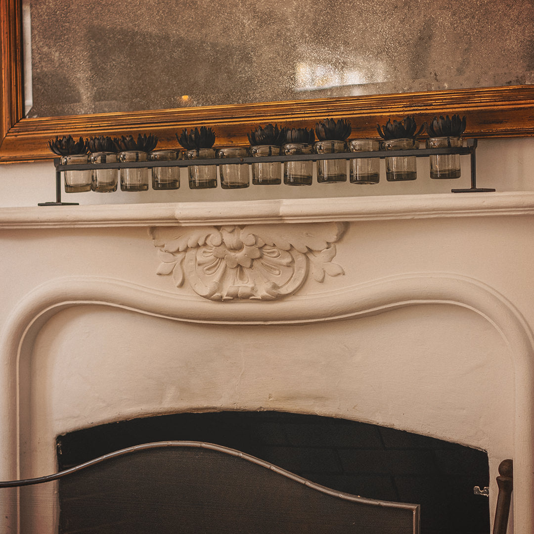 Wax cast railroad with mouth blown glass votive holders on a forged iron stand. Iron flowers on top of the glasses. On top of a white chimney.