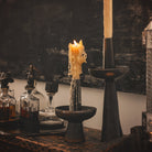 Two  iron primitive and sculptural candlesticks with a candle each. Next to several decanters with iron toppers.