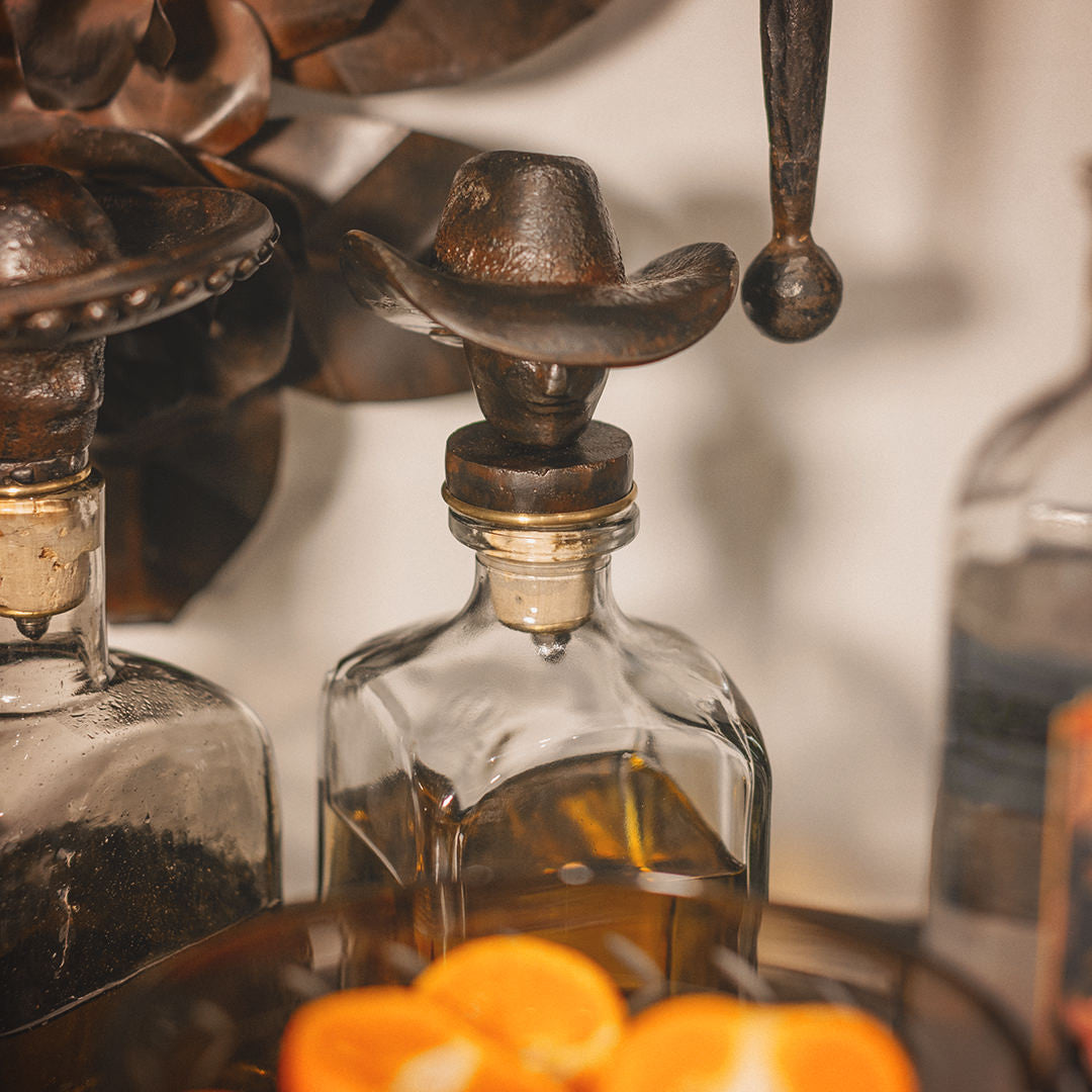 A cowboy iron decanter topper with vintage style glass bottle surrounded by other unfocused objects.