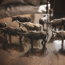 Several  longhorn bull iron sculptures and other longhorn bull nickel plated sculptures on top of a wooden table.