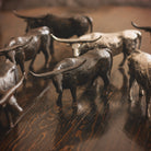 Several  longhorn bull iron sculptures and other longhorn bull nickel plated sculptures on top of a wooden table.