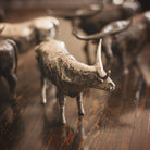 A  nickel plated longhorn bull  iron sculpture in front of other iron longhorn sculptures. Wood floor.