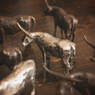 A  nickel plated longhorn bull  iron sculpture surrounded by  other iron longhorn sculptures. Wood floor.