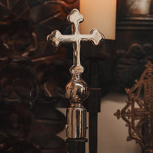 A nickel plated cross. In the background several iron flowers and objects can be seen.