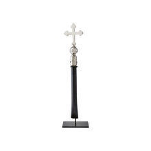 A nickel plated cross with natural iron handle supported on a gallery stand.