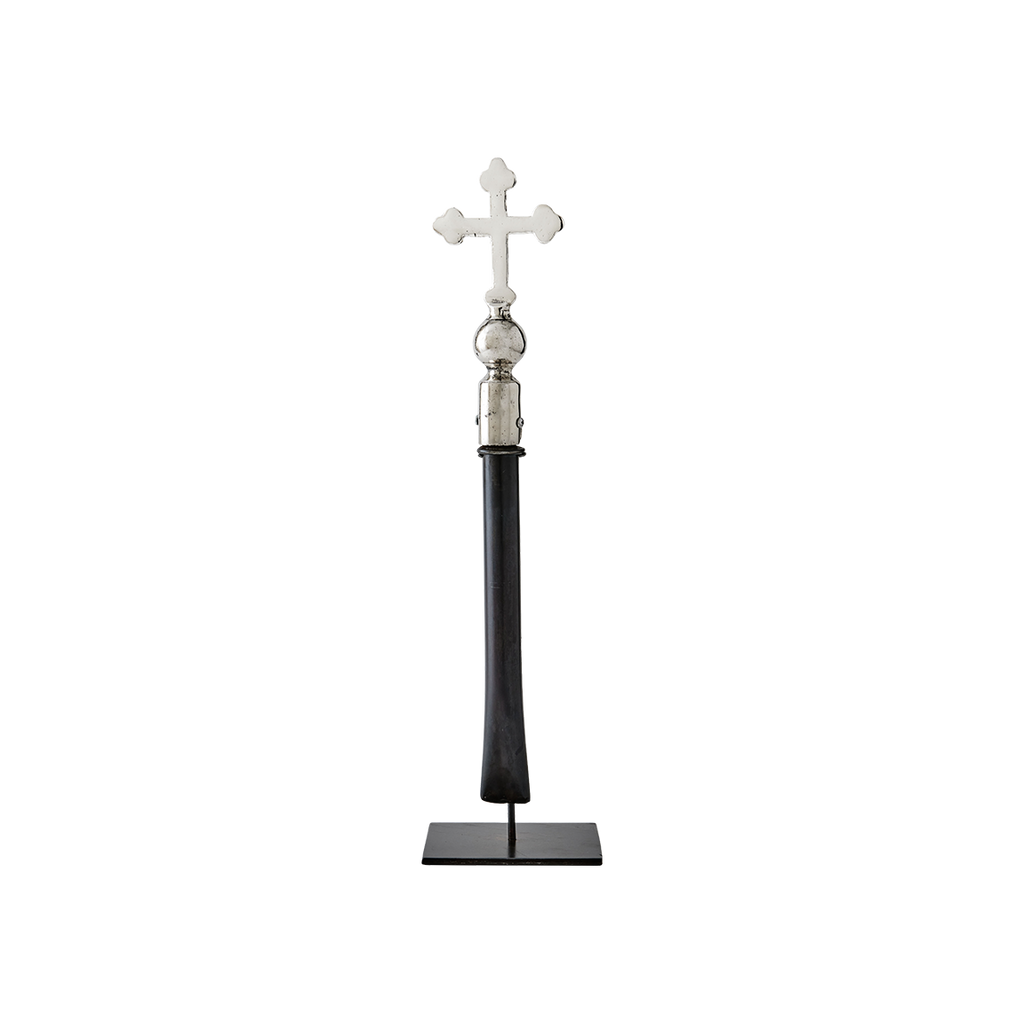 A nickel plated cross with natural iron handle supported on a gallery stand.