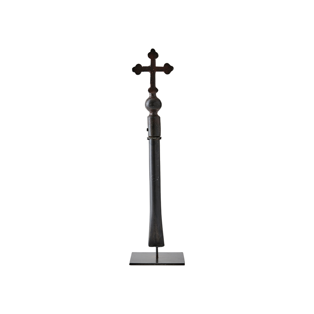 A natural cast iron cross with handle supported on a gallery stand.