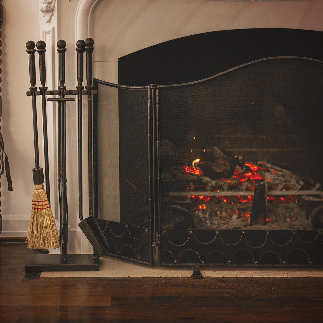 A lit white chimney with a fire screen and to the left a set of tools